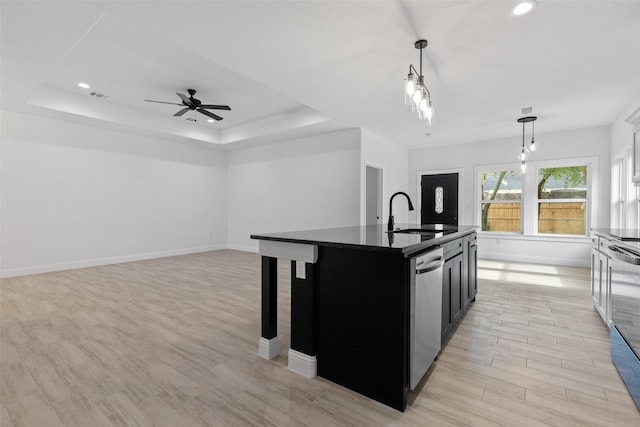 kitchen featuring pendant lighting, sink, dishwasher, a tray ceiling, and a center island with sink