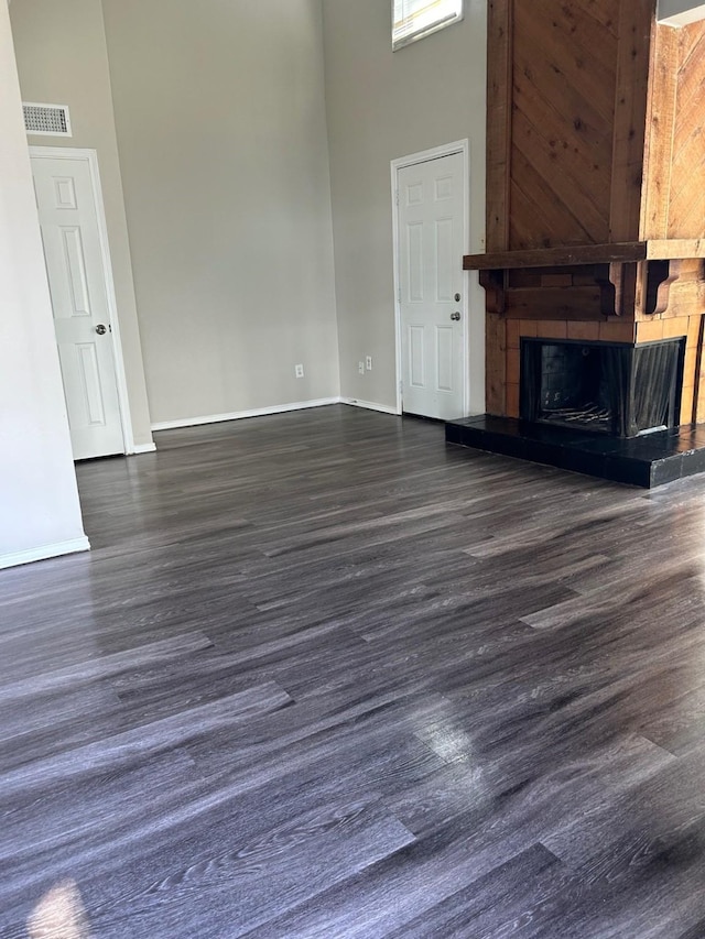 unfurnished living room with dark wood-type flooring, a towering ceiling, and a large fireplace