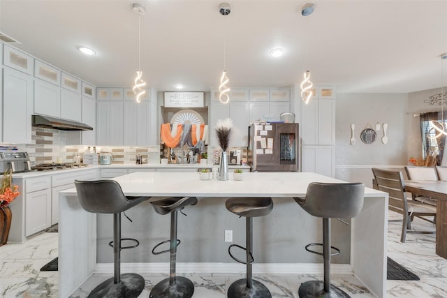 kitchen featuring pendant lighting, a center island with sink, range hood, white cabinetry, and a breakfast bar area