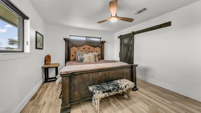 bedroom with a barn door, ceiling fan, multiple windows, and light wood-type flooring