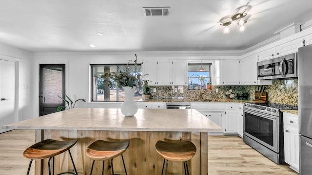 kitchen featuring white cabinetry, a center island, stainless steel appliances, a kitchen bar, and light wood-type flooring