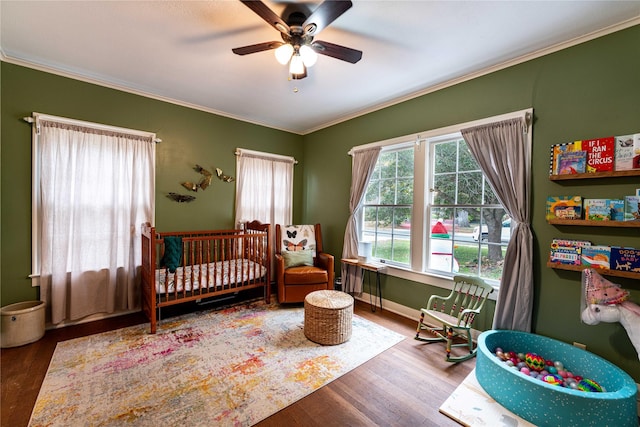 bedroom featuring ceiling fan, ornamental molding, hardwood / wood-style floors, and a crib