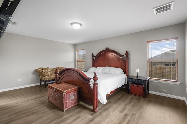 bedroom with visible vents, baseboards, wood finished floors, and multiple windows