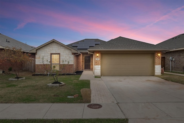 ranch-style home featuring an attached garage, a front lawn, roof mounted solar panels, and stone siding