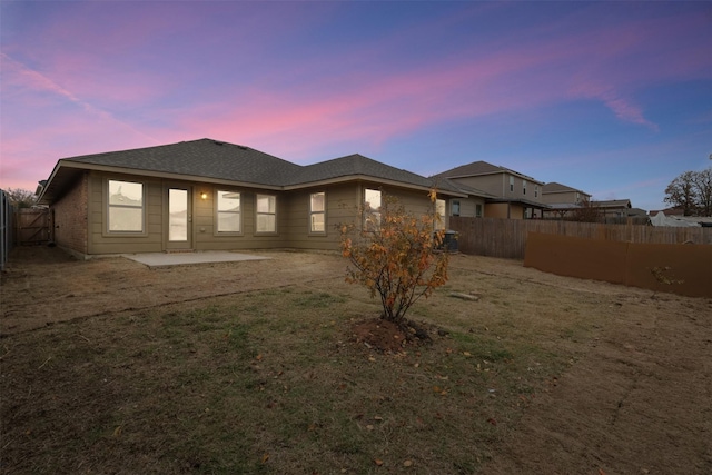 back of property at dusk featuring a yard, a patio, and a fenced backyard