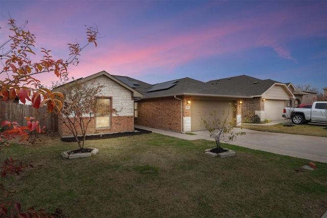 ranch-style home featuring driveway, brick siding, an attached garage, a yard, and solar panels