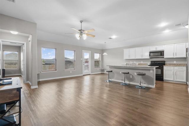 kitchen with dark wood-type flooring, black electric range, an island with sink, pendant lighting, and white cabinets