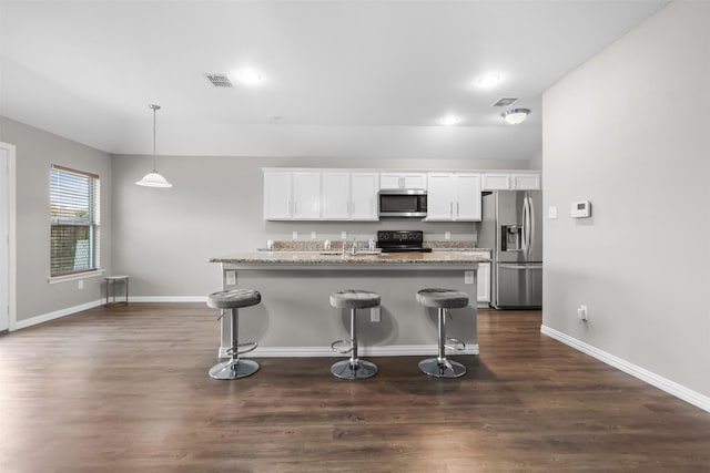 kitchen with an island with sink, appliances with stainless steel finishes, dark hardwood / wood-style flooring, white cabinetry, and a breakfast bar area