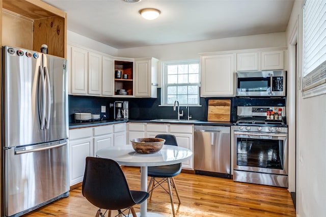 kitchen featuring backsplash, light wood-type flooring, stainless steel appliances, sink, and white cabinetry