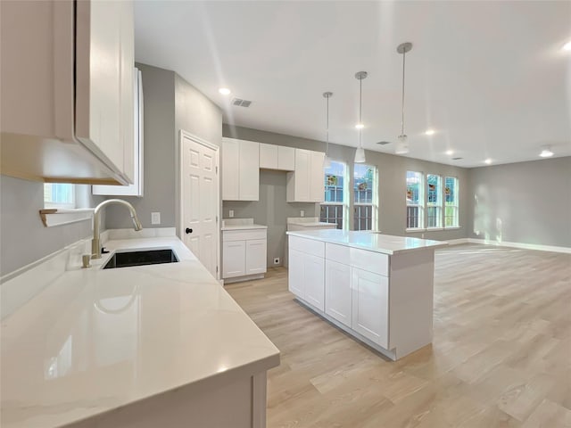 kitchen featuring a kitchen island, sink, decorative light fixtures, light hardwood / wood-style floors, and white cabinetry