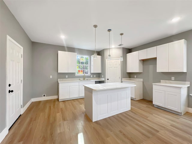 kitchen featuring sink, hanging light fixtures, white cabinets, a kitchen island, and light wood-type flooring