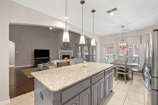 kitchen featuring lofted ceiling, light stone counters, a chandelier, stainless steel fridge, and a fireplace