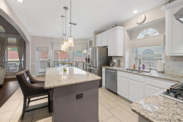 kitchen featuring appliances with stainless steel finishes, decorative light fixtures, white cabinetry, sink, and a center island