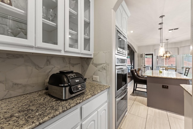 kitchen with stainless steel appliances, hanging light fixtures, white cabinets, and light stone counters