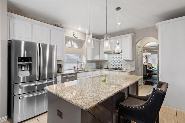 kitchen with sink, stainless steel appliances, a center island, light stone countertops, and white cabinets