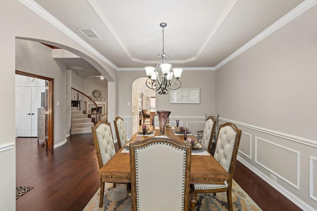 dining room with dark wood-type flooring, ornamental molding, a tray ceiling, and an inviting chandelier