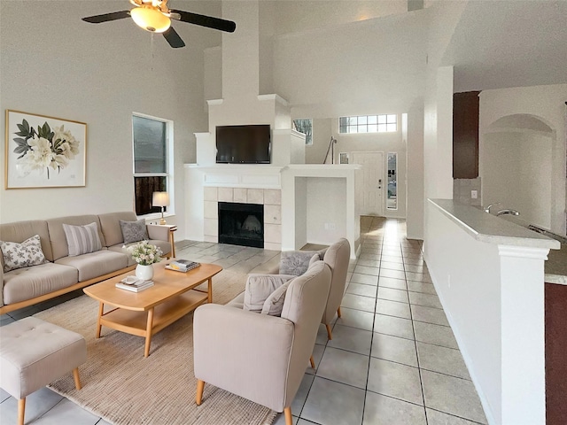 living room with a tile fireplace, light tile patterned floors, high vaulted ceiling, and ceiling fan