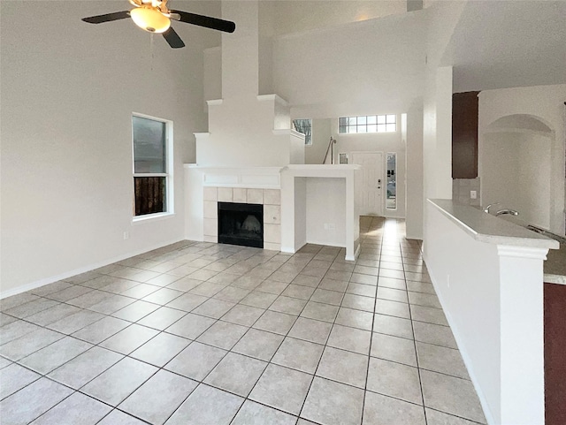 unfurnished living room with a tile fireplace, ceiling fan, high vaulted ceiling, and light tile patterned flooring