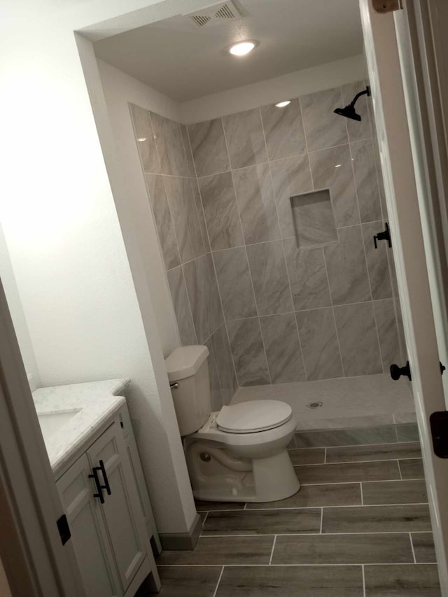 bathroom featuring tiled shower, vanity, and toilet