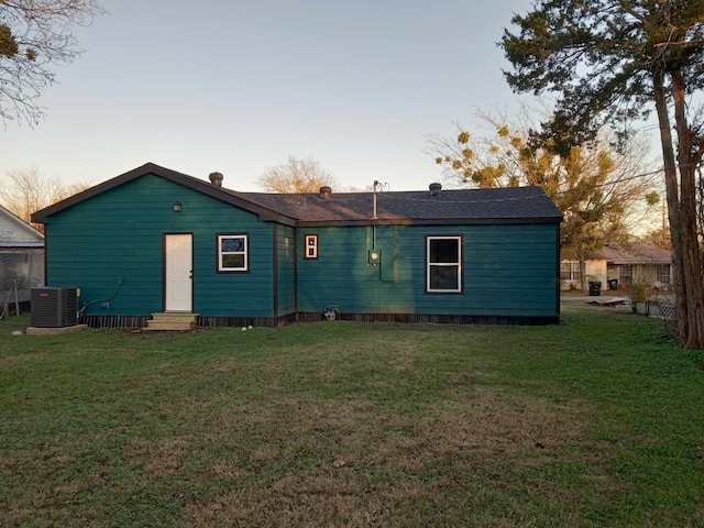 back house at dusk featuring a yard and central air condition unit