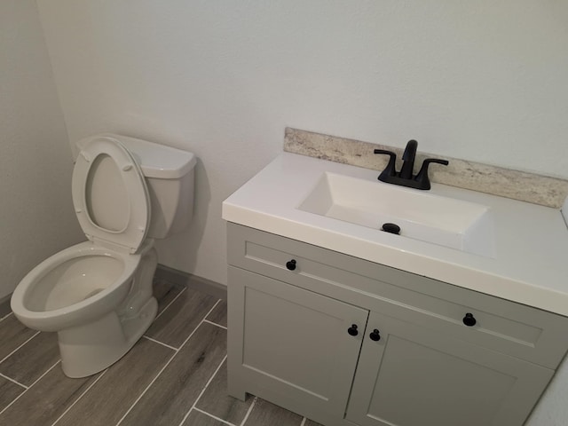 bathroom with wood finish floors, baseboards, toilet, and vanity