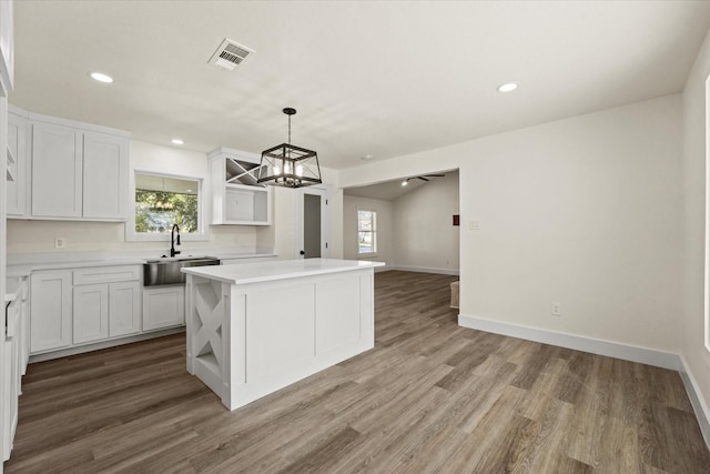 kitchen with pendant lighting, white cabinets, a center island, hardwood / wood-style floors, and sink