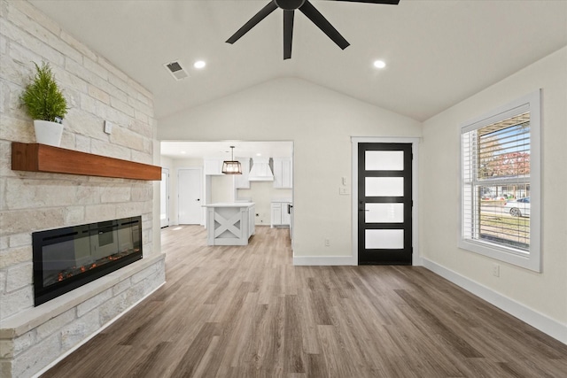 unfurnished living room with ceiling fan, light hardwood / wood-style floors, a stone fireplace, and vaulted ceiling