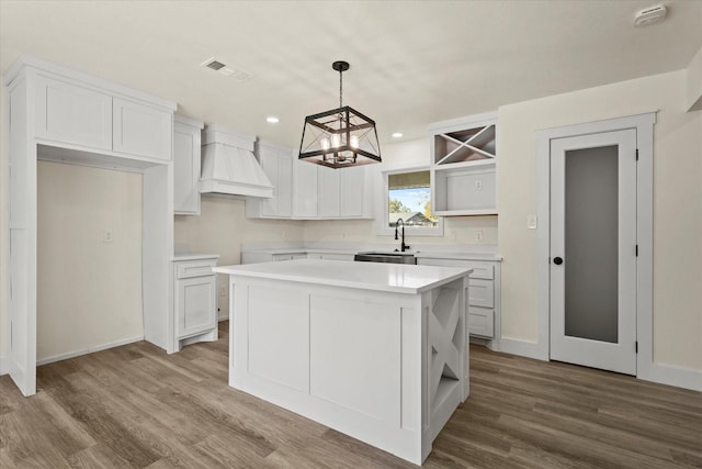 kitchen featuring a center island, sink, hanging light fixtures, custom range hood, and white cabinets