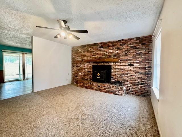 unfurnished living room featuring carpet flooring, a textured ceiling, a wood stove, and ceiling fan