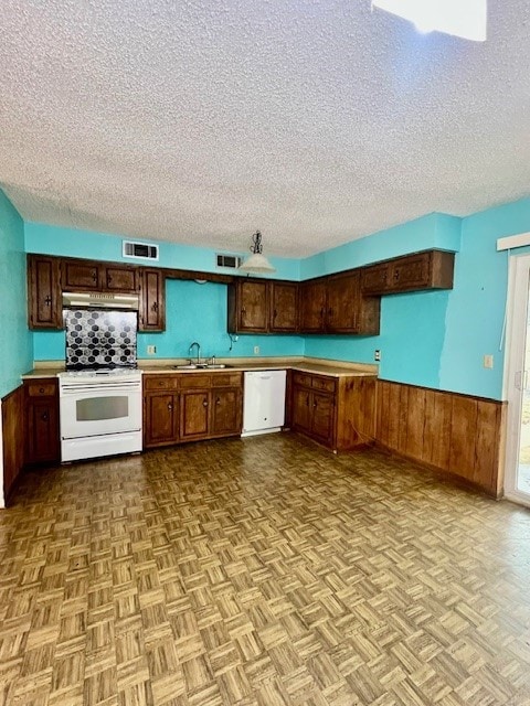 kitchen featuring wood walls, sink, light parquet floors, white appliances, and a textured ceiling