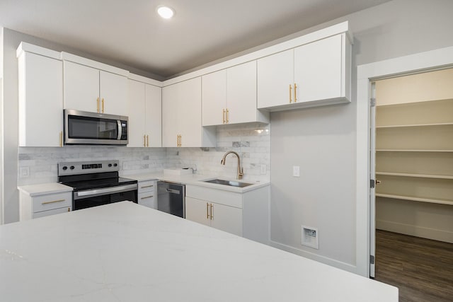 kitchen with appliances with stainless steel finishes, tasteful backsplash, dark wood-type flooring, sink, and white cabinetry