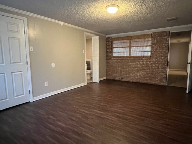 unfurnished room with dark hardwood / wood-style flooring, ornamental molding, a textured ceiling, and brick wall