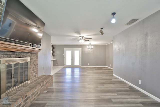 unfurnished living room with french doors, a brick fireplace, crown molding, ceiling fan with notable chandelier, and hardwood / wood-style flooring