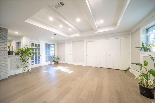 unfurnished living room with a healthy amount of sunlight, light hardwood / wood-style floors, and a tray ceiling