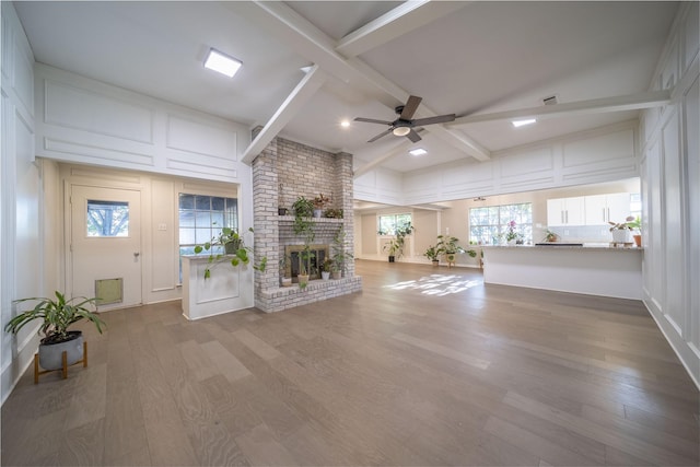 unfurnished living room featuring hardwood / wood-style floors, ceiling fan, vaulted ceiling with beams, and a brick fireplace