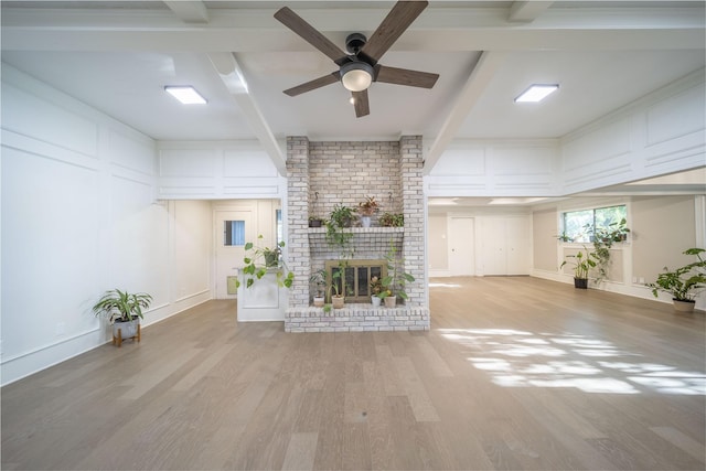 unfurnished living room with ceiling fan, a fireplace, beamed ceiling, and light wood-type flooring