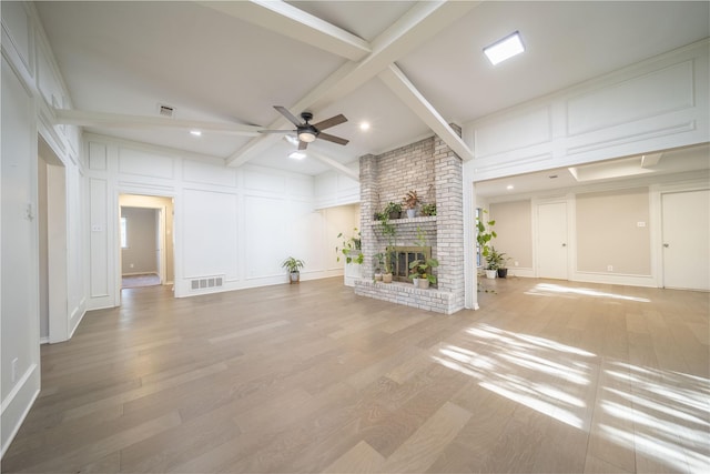 unfurnished living room with beamed ceiling, hardwood / wood-style floors, a brick fireplace, and ceiling fan