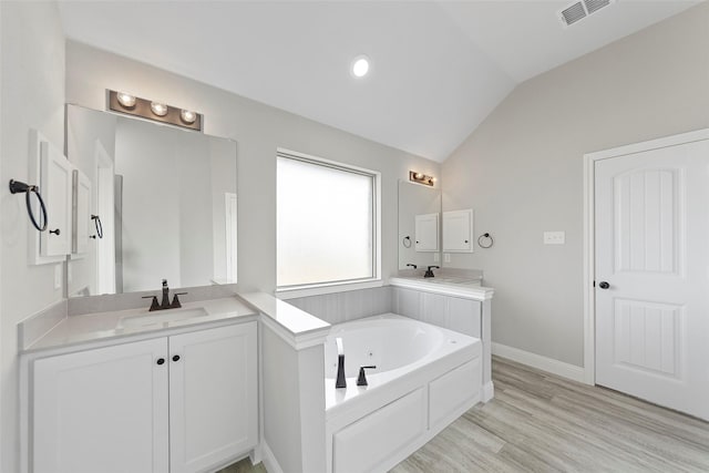 bathroom featuring hardwood / wood-style floors, vanity, lofted ceiling, and a washtub