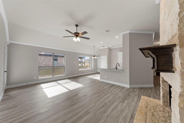 unfurnished living room with ceiling fan, sink, crown molding, light hardwood / wood-style floors, and a fireplace