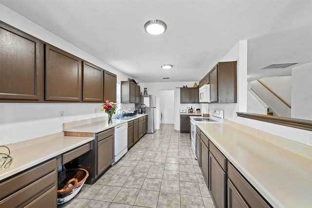 kitchen featuring light tile patterned flooring, dark brown cabinetry, white appliances, and sink