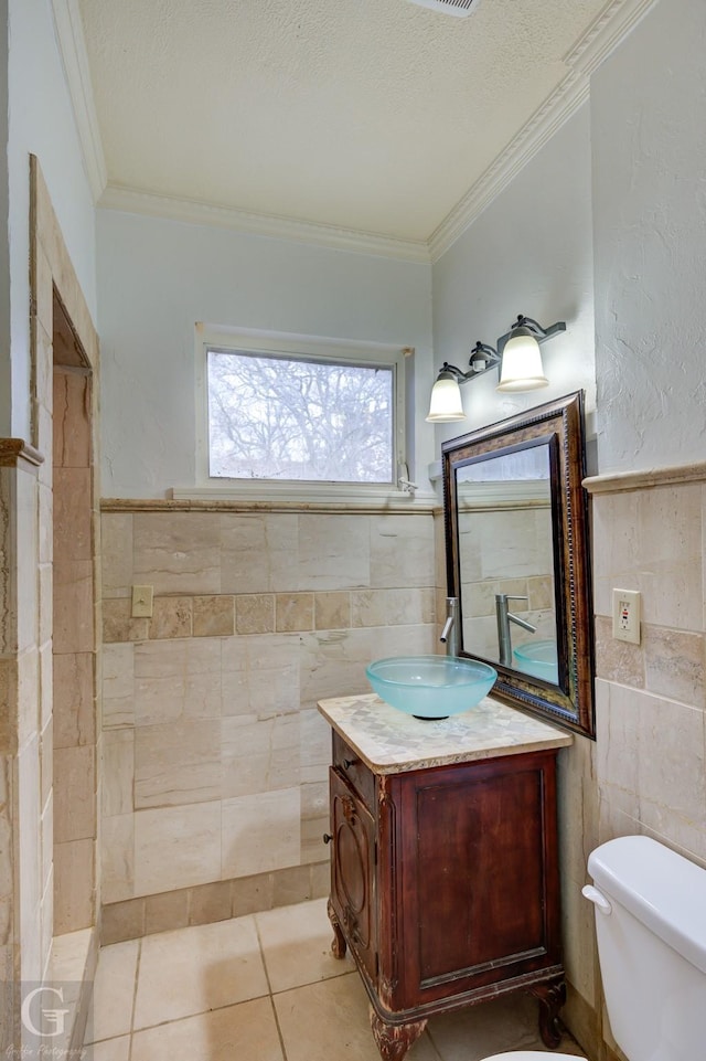 bathroom with vanity, tile patterned flooring, toilet, ornamental molding, and tile walls