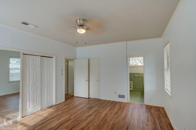 unfurnished bedroom with hardwood / wood-style floors, multiple closets, ceiling fan, and ornamental molding