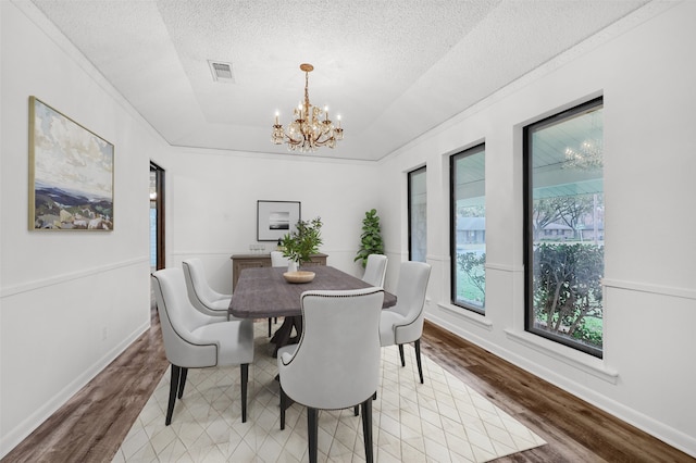 dining space featuring a raised ceiling, hardwood / wood-style floors, a textured ceiling, and a notable chandelier