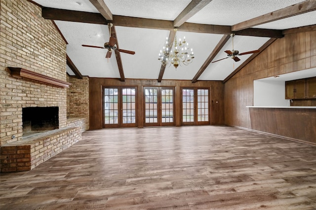 unfurnished living room featuring a fireplace, wood walls, wood-type flooring, ceiling fan, and a textured ceiling