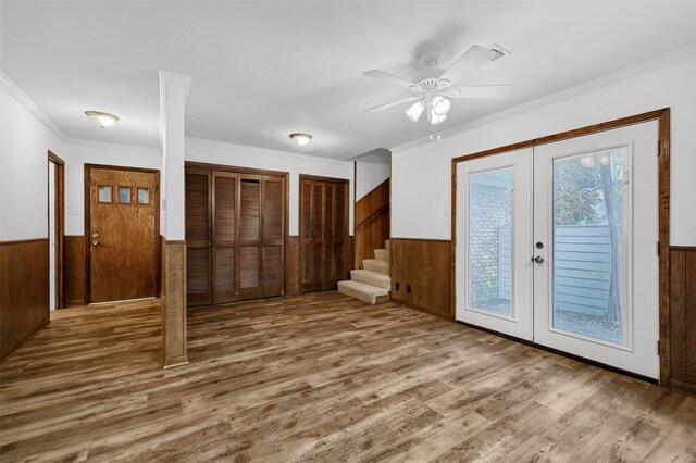 foyer with ceiling fan, wooden walls, wood-type flooring, ornamental molding, and french doors