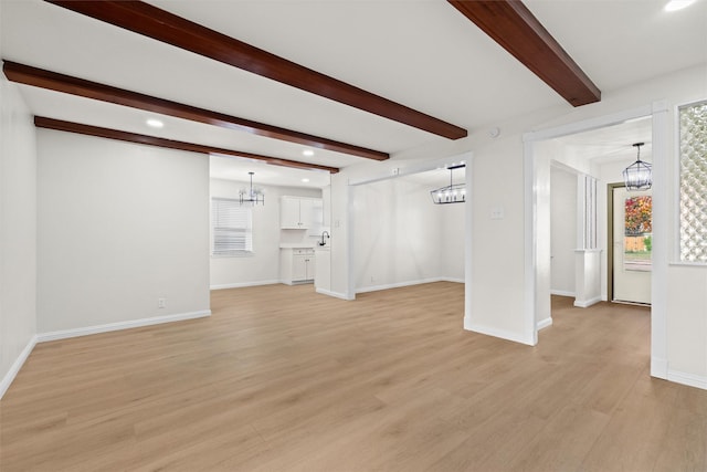 unfurnished living room featuring beamed ceiling, light hardwood / wood-style flooring, and sink