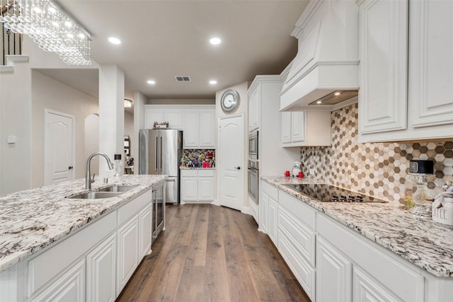 kitchen with appliances with stainless steel finishes, white cabinetry, sink, hanging light fixtures, and custom range hood