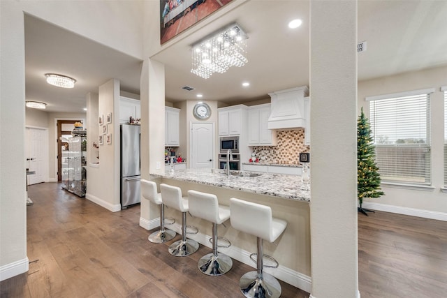 kitchen with appliances with stainless steel finishes, hardwood / wood-style floors, white cabinetry, a kitchen breakfast bar, and light stone countertops