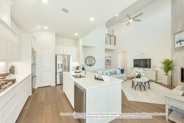 kitchen featuring sink, appliances with stainless steel finishes, a kitchen island with sink, white cabinets, and light wood-type flooring