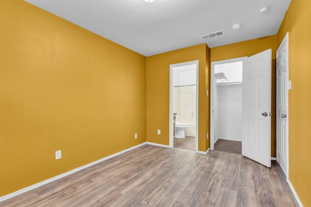 unfurnished bedroom featuring a walk in closet, connected bathroom, light hardwood / wood-style floors, and a closet